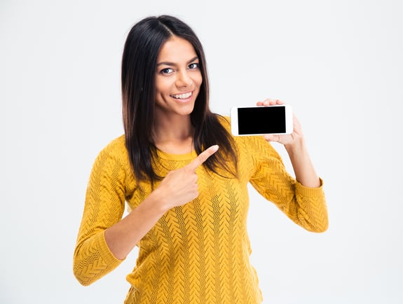 Cheerful cute woman pointing finger on smartphone screen isolated on a white background. Looking at camera